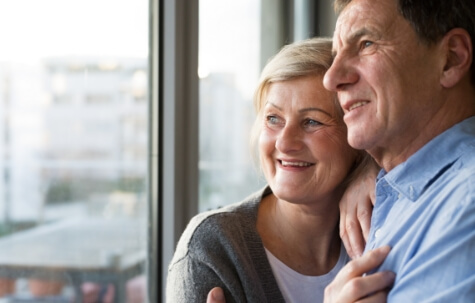 senior couple in living room standing at the window hugging